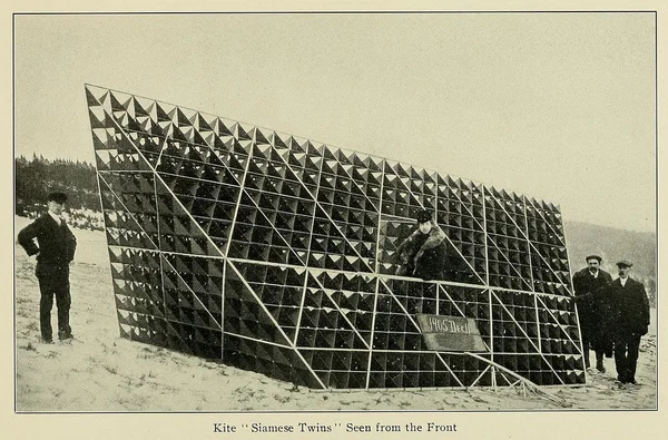The Siamese Twins kite seen from the front — a wall of hundreds of tetrahedral cells standing in snow, with four men beside it for scale