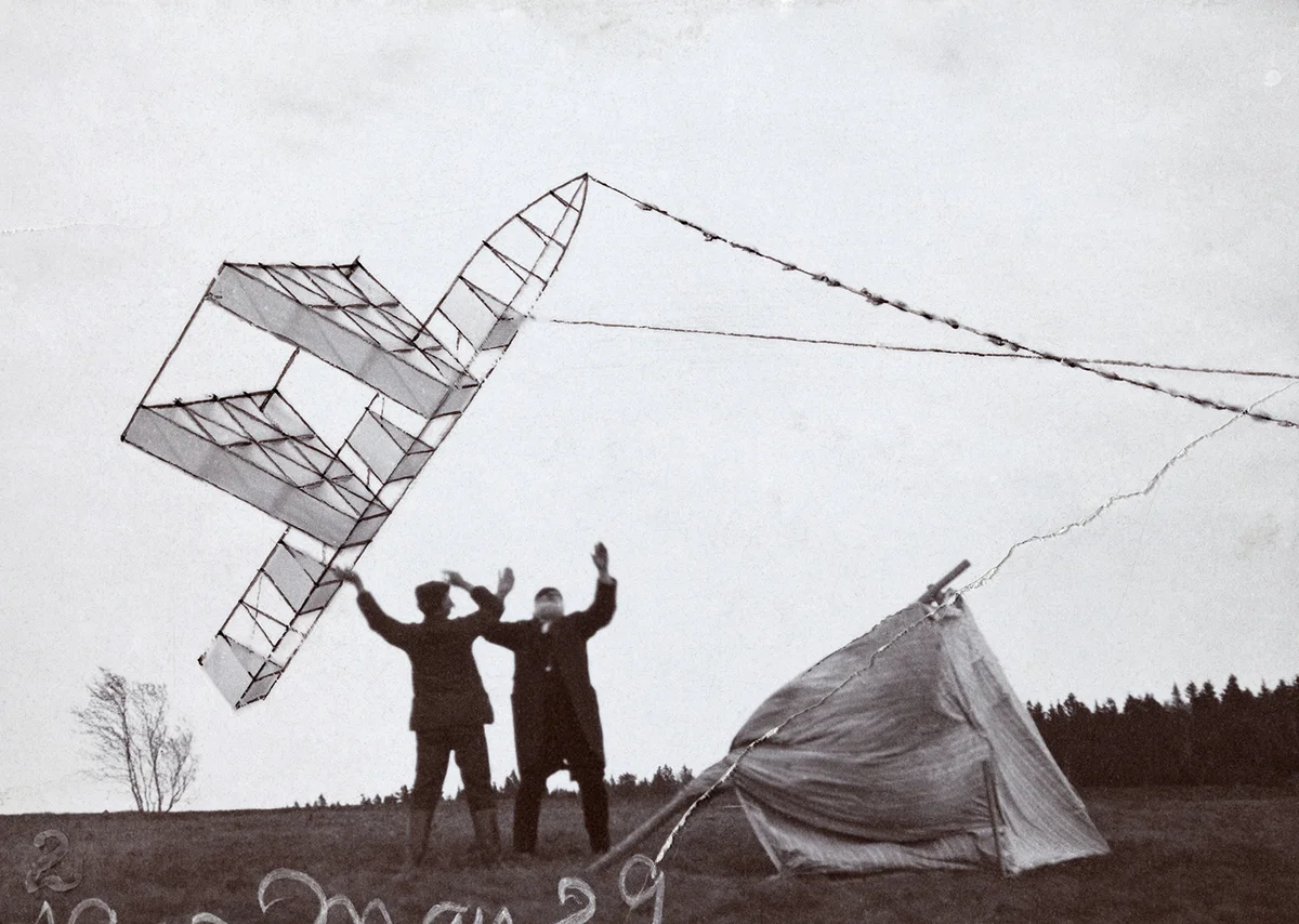 Two men with their arms raised releasing a large kite into the wind at Beinn Bhreagh, a canvas tent beside them