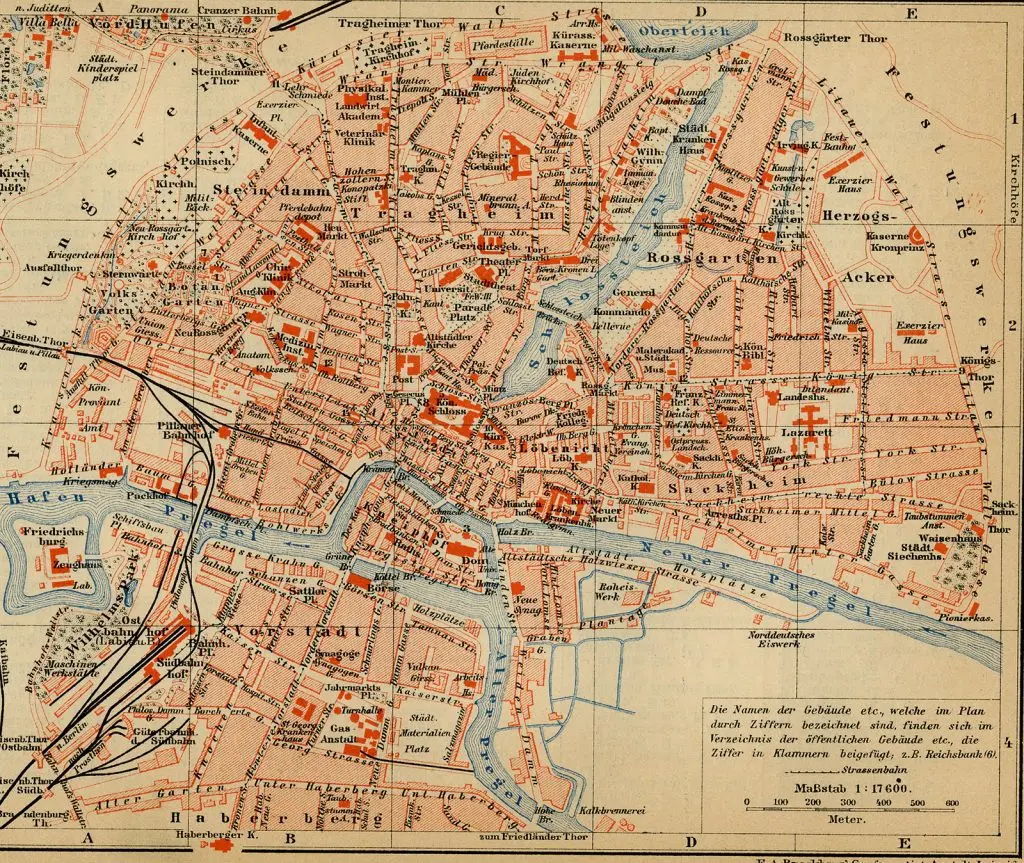 Old colour city map of Königsberg: dense streets in red and cream, the blue Pregel river splitting around a central island with the cathedral, bridges crossing both arms, and railway lines to the south-west